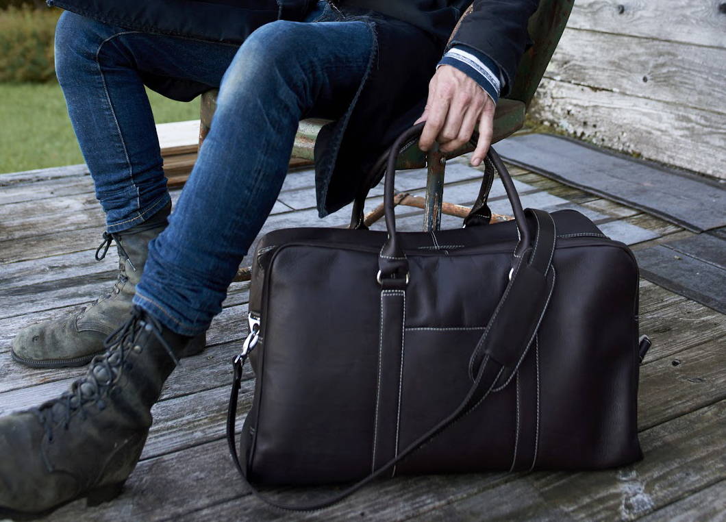 Man sitting outdoors holding a leather duffel bag